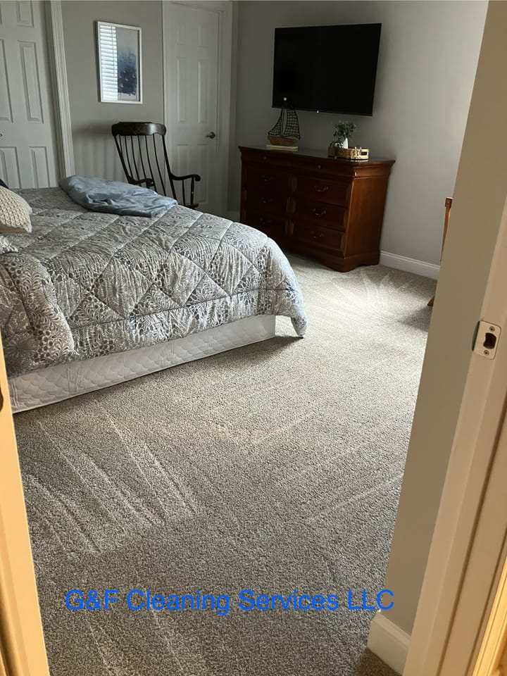 A bedroom with the bed made and carpet vacuumed